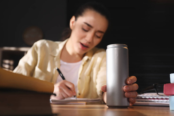 Tired young woman with energy drink studying at home, focus on hand - Фото, зображення