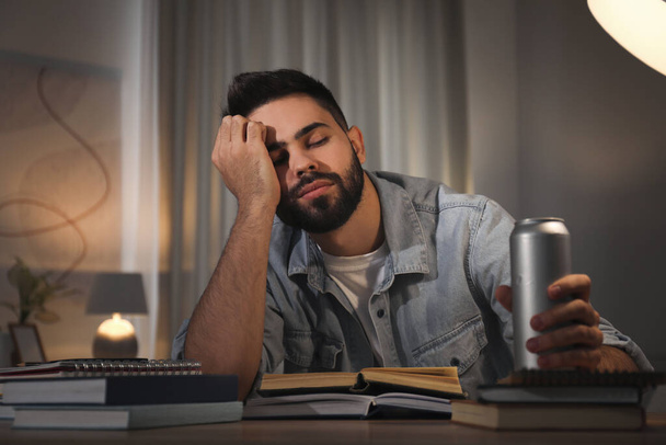 Втомлений молодий чоловік з енергетичним напоєм навчається вдома
 - Фото, зображення