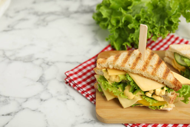 Ξύλινη σανίδα με νόστιμο σάντουιτς σε λευκό μαρμάρινο τραπέζι, χώρος για κείμενο - Φωτογραφία, εικόνα