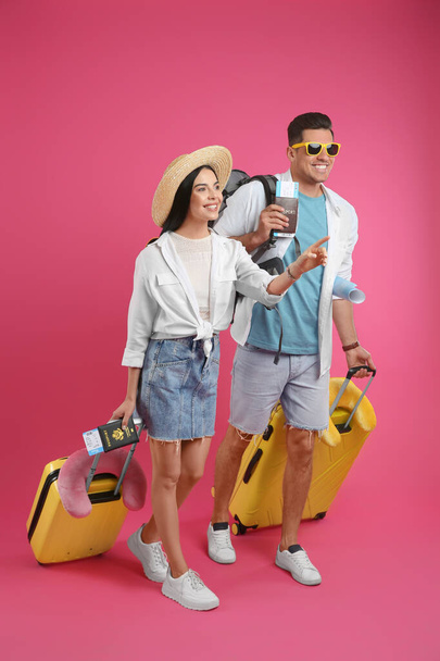 Couple of tourists with tickets, passports and suitcases on pink background - Foto, afbeelding