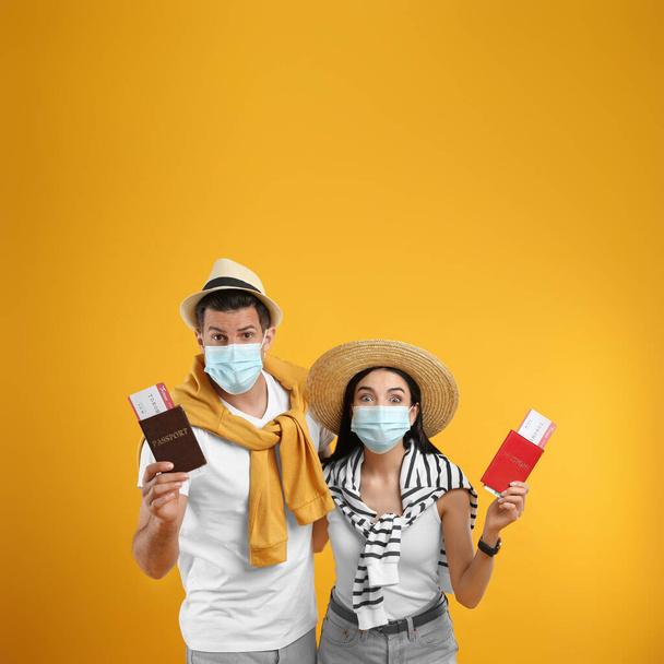 Couple of tourists in medical masks with tickets and passports on yellow background. Travelling during coronavirus pandemic - Foto, immagini