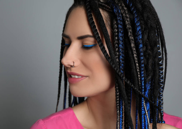 Beautiful young woman with nose piercing and dreadlocks on grey background - Φωτογραφία, εικόνα