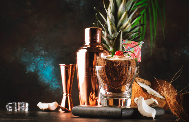 Pina Colada Summer Cocktail in chopped coconut with tropical fruits and copper bar tools, copy space - Foto, Imagem