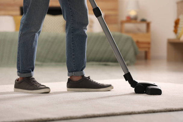Man cleaning carpet with vacuum cleaner at home, closeup - Фото, изображение