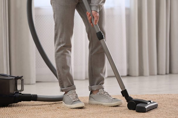 Man cleaning carpet with vacuum cleaner at home, closeup - Foto, afbeelding