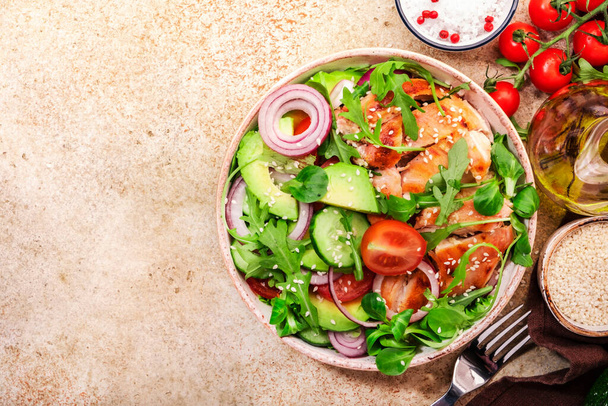 Grilled chicken salad with tomatoes, arugula, red onion, avocado, sesame seeds and lemon oil dressing. Healthy food. Beige background. Top view - Foto, Imagem
