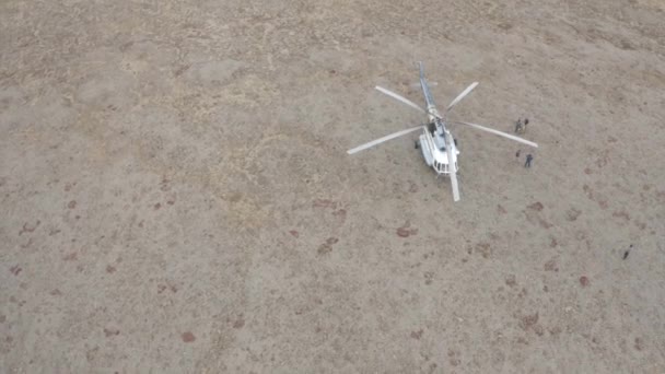 Aerial top view of a helicopter on dry ground arrived to rescue a small group of people. Clip. Saving tourists lost in wild nature. - Footage, Video
