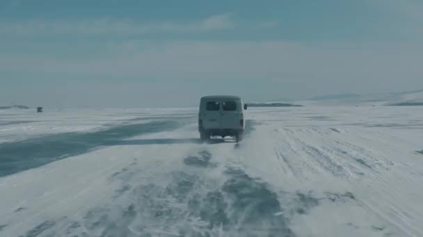 View through the windshield of a car on a convoy of UAZ minibuses on the icy road of Lake Baikal under a clear sunny sky - Footage, Video