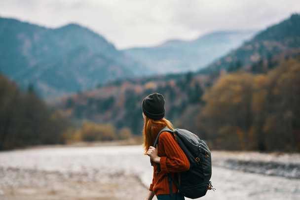 жінка в капелюсі з рюкзаком відпочиває в горах на природі біля річки
 - Фото, зображення