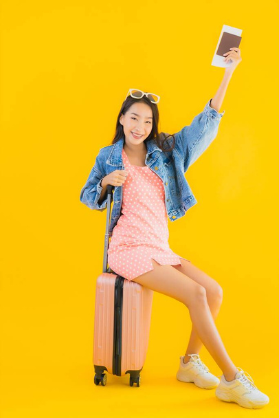 Çantalı güzel Asyalı kadın. Pasaportu ve sarı izole bir arka planda bilet. - Fotoğraf, Görsel