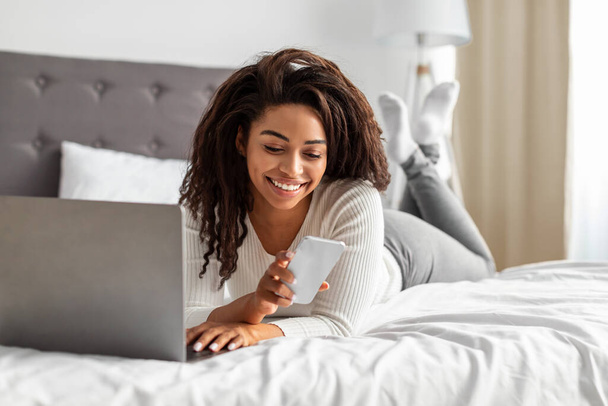 Happy black woman lying in bed reading text message - Valokuva, kuva