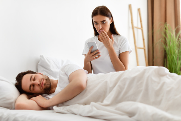 Zszokowana żona czytanie wiadomości na temat zdradzających mężów Smartphone w sypialni - Zdjęcie, obraz