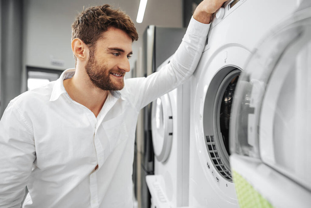 Young man choosing new washing machine in household appliances store - Фото, изображение
