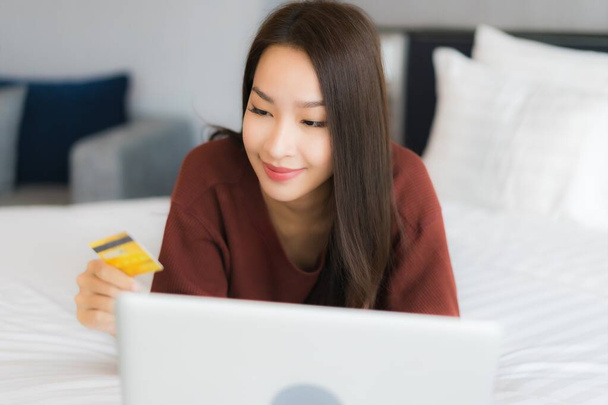 Portret mooie jonge aziatische vrouw gebruik computer laptop op bed in slaapkamer interieur - Foto, afbeelding