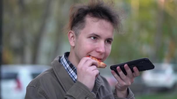 Ragazzo mangiare pizza e inviare messaggi vocali su smartphone in città - Filmati, video