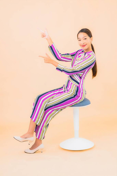 Güzel bir Asyalı kadın portresi. Sandalyeye otur ve renkli arka planda gülümse. - Fotoğraf, Görsel