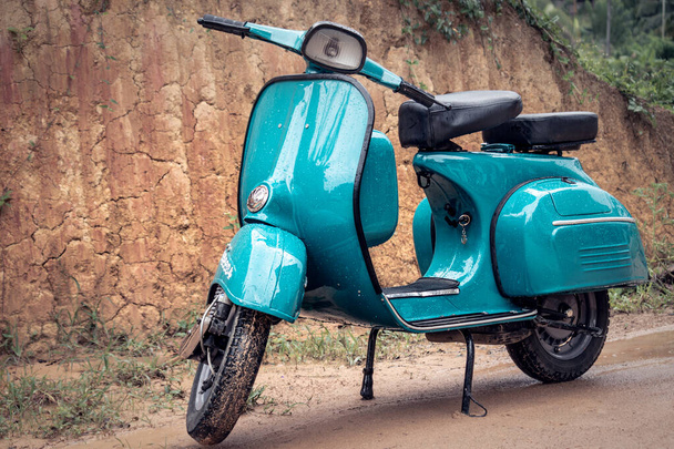 Vespa Scooter vooraanzicht, geparkeerd in een modderige weg op een regenachtige dag. Sky blauwe vintage klassieke motorfiets. - Foto, afbeelding