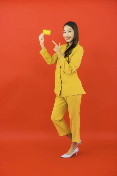 Güzel bir Asyalı kadının portresi kırmızı arka planda kredi kartıyla cep telefonu kullanıyor. - Fotoğraf, Görsel