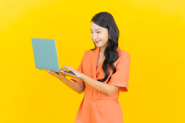Retrato hermosa joven asiática mujer sonrisa con ordenador portátil en amarillo aislado fondo - Foto, imagen
