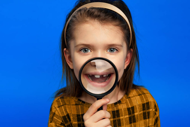Девушка ярко улыбается через лупу, изолированную на синем фоне - Фото, изображение