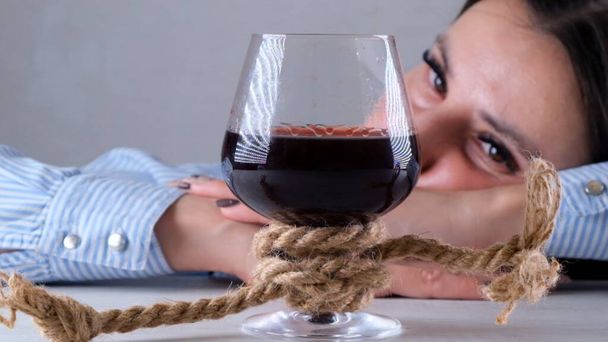 Грустная женщина, выглядящая как бокал вина, связанный джутовой веревкой. Концепция алкогольной зависимости. Проблема лечения алкоголизма - Фото, изображение