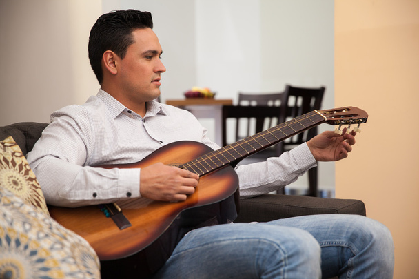 atraktivní mladý muž ladění jeho kytara hrála doma pár písniček - Fotografie, Obrázek