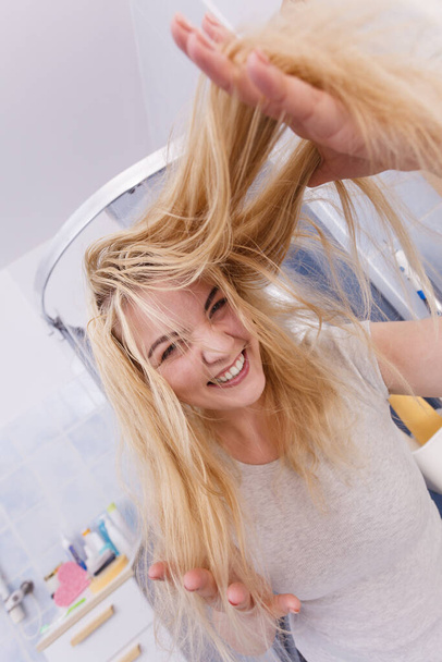 Happy woman in bathroom having wet long blonde hair. Playful young teenage female taking care of her hairdo. - Photo, Image
