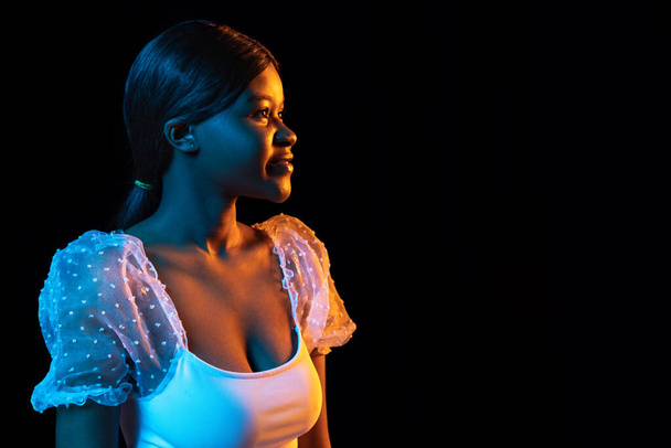 One young African beautiful girl isolated over dark background in mixed neon light. - Foto, Bild