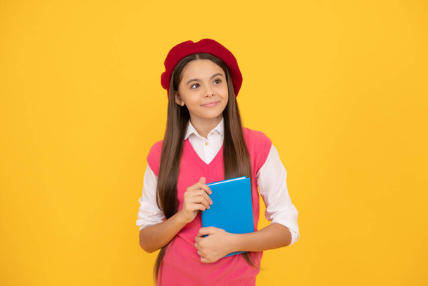 glücklich Teenager Schulmädchen in Französisch Baskenmütze halten Werbebuch auf gelbem Hintergrund, Literatur. - Foto, Bild