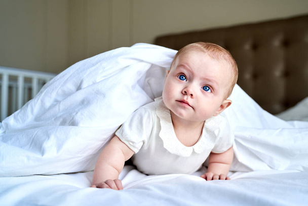 a small child with blue eyes lies on a white bed. - Foto, immagini