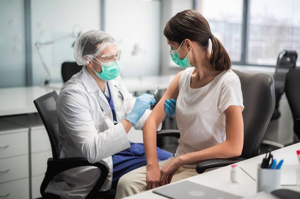 Mladá žena v masce se rozhodla nechat se očkovat proti koronaviru během pandemie zkušeným lékařem v laboratoři - Fotografie, Obrázek