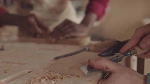 Rackerte Fokusaufnahme von zwei nicht wiederzuerkennenden multiethnischen Zimmerleuten, die in der Tischlerei Holzstücke mit Meißeln schnitzen - Filmmaterial, Video
