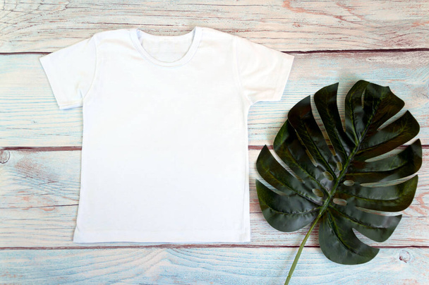 White t-shirt mockup with monstera on wooden background, top view. - Photo, Image