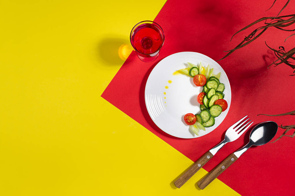 Raw healthy salad - red tomatoes, cucumber, celery on white plate in hard light, shadow, drink on modern geometric red, yellow background, flat lay. - Photo, Image