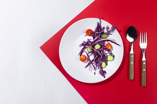 Raw healthy salad with purple cabbage, red tomatoes, cucumber on white plate in hard light with shadow on modern geometric red color, white wood background. - Photo, image