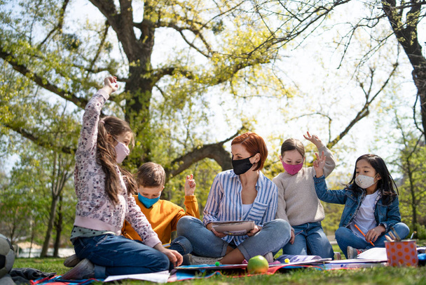 Teacher with small children sitting outdoors in city park, learning group education and coronavirus concept. - Foto, Imagem