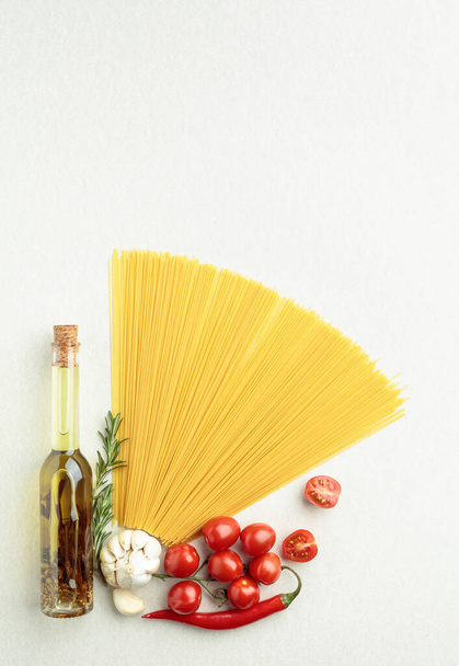 Спагетти с бутылкой оливкового масла, перцем, чесноком, помидорами и розмарином, вид сверху. - Фото, изображение