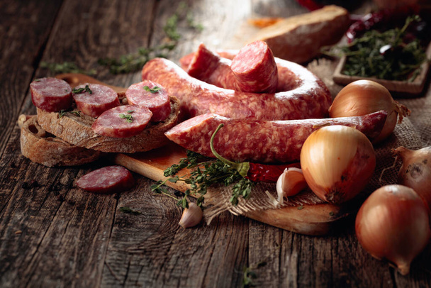 Dry-cured sausages with herbs and spices. Sausages with bread, thyme, pepper, onion, and garlic on an old wooden table. Simple healthy food. - Foto, Bild