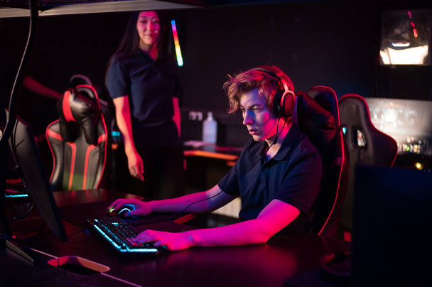 A young asian girl flirts with a guy in a computer club, she smiles and offers help in the game - Valokuva, kuva