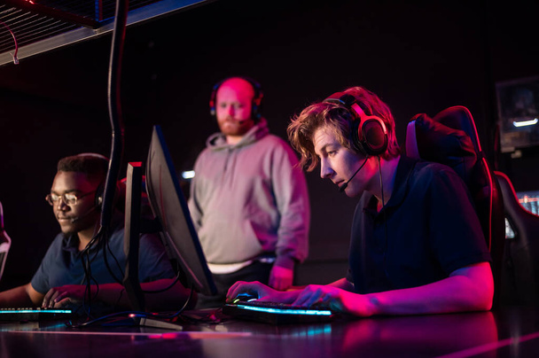 During the Dota 2 tournament, two guys from the team play at the computers, the coach watches from behind - Photo, Image