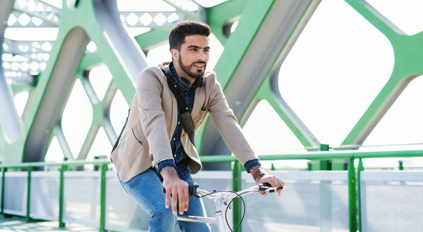 Young business man commuter with bicycle going to work outdoors in city, riding on bridge. - Φωτογραφία, εικόνα