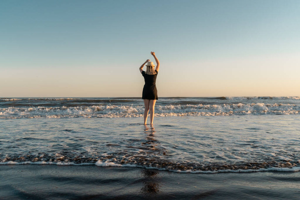 Szczęśliwa kobieta na brzegu plaży o zachodzie słońca tańcząca z ramionami w powietrzu.  - Zdjęcie, obraz
