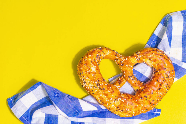 Oktoberfest concept - pretzel on a traditional napkin. Trendy hard light, dark shadow. Pastel yellow background, top view - Photo, Image