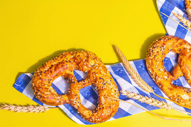 El concepto Oktoberfest - los pretzels sobre la servilleta tradicional. Luz dura de moda, sombra oscura. Espiguillas secas, fondo amarillo pastel, lugar para texto - Foto, Imagen