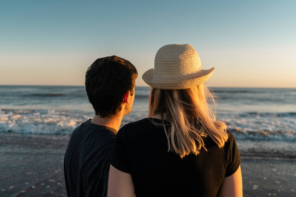 Fiatal pár szerelmes a tengerparton nézi a naplementét. - Fotó, kép