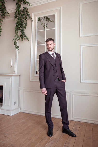 beautiful young man with a beard brunette model. guy in a classic suit in a light stylish interior. groom. portrait - Valokuva, kuva