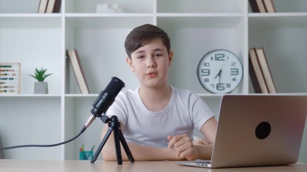 男の子vloggerは、カメラを見て、インターネット用のポッドキャストビデオを記録します。子供のビデオブロガーは自宅でプロのマイクで新しいvlogビデオを撮影.若いブロガービデオ撮影について話す. - 映像、動画