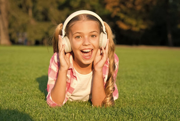 small girl listen audio book. new technology for kids. happy childhood memories. listening to music. back to school. kid study in park. relax on green grass in headphones. Hooked On Learning. - Foto, imagen