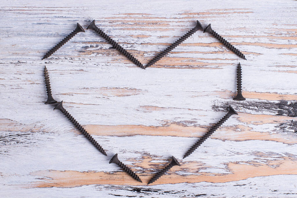 Форма сердца от черных винтов на деревянном фоне. - Фото, изображение