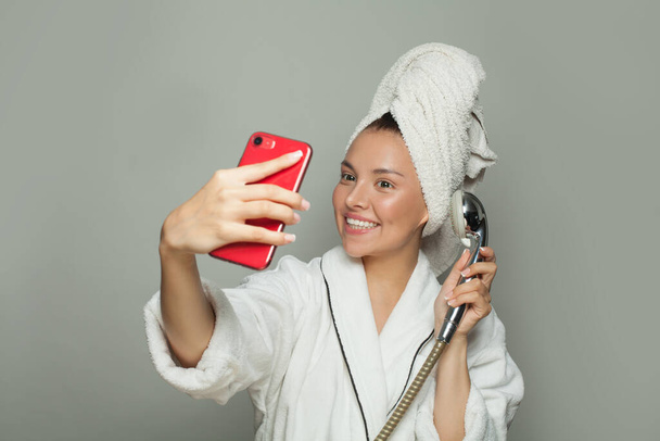 Szczęśliwa atrakcyjna kobieta bierze prysznic i robi selfie na szarym tle - Zdjęcie, obraz